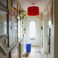 narrow hallway with art on the walls and bright red lightshade