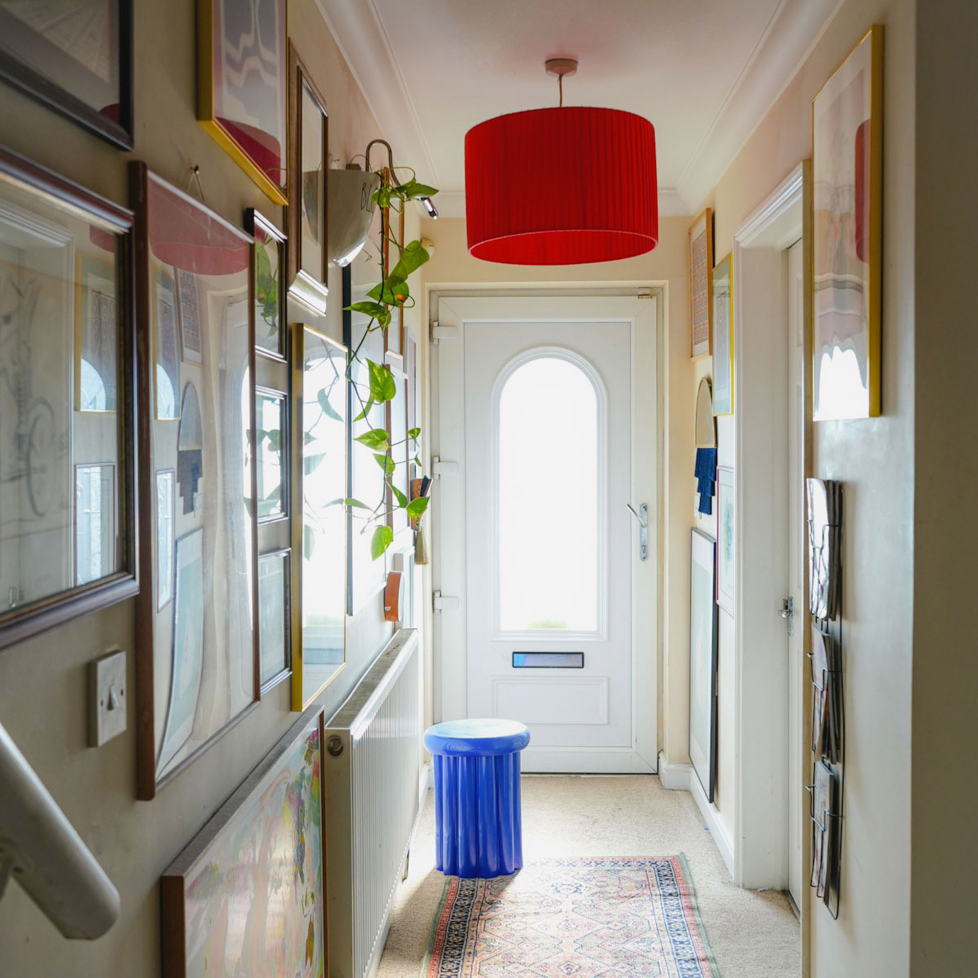 narrow hallway with art on the walls and bright red lightshade