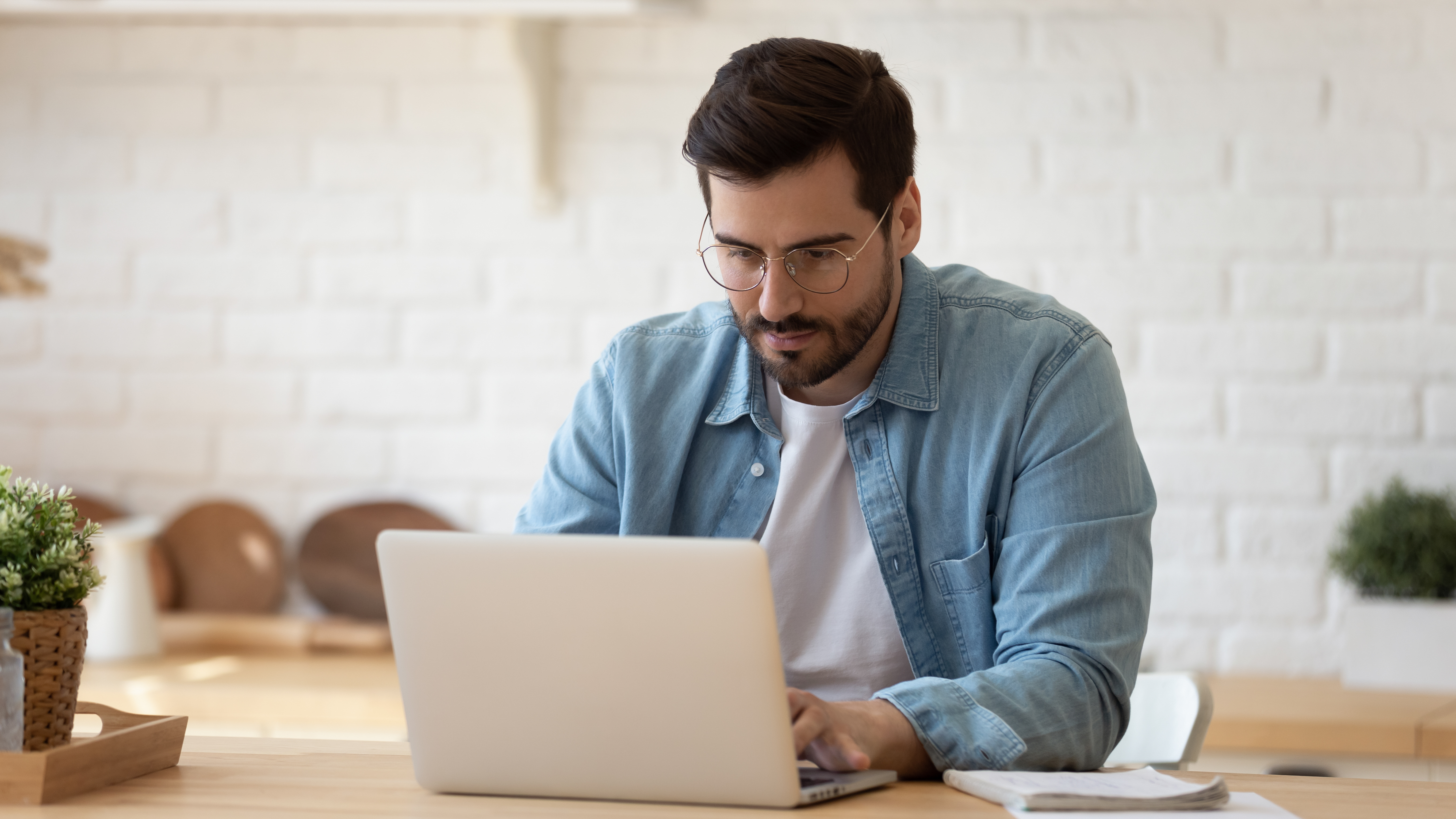 Man wearing glasses, sitting at a table and using a laptop