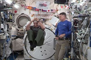 NASA astronaut Mark Vandei Hei demonstrates orbital acrobatics as his Expedition 65 crewmate Shane Kimbrough looks on during an educational downlink from the International Space Station.