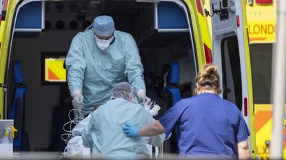 NHS workers in PPE take a patient from an ambulance at St Thomas' Hospital.