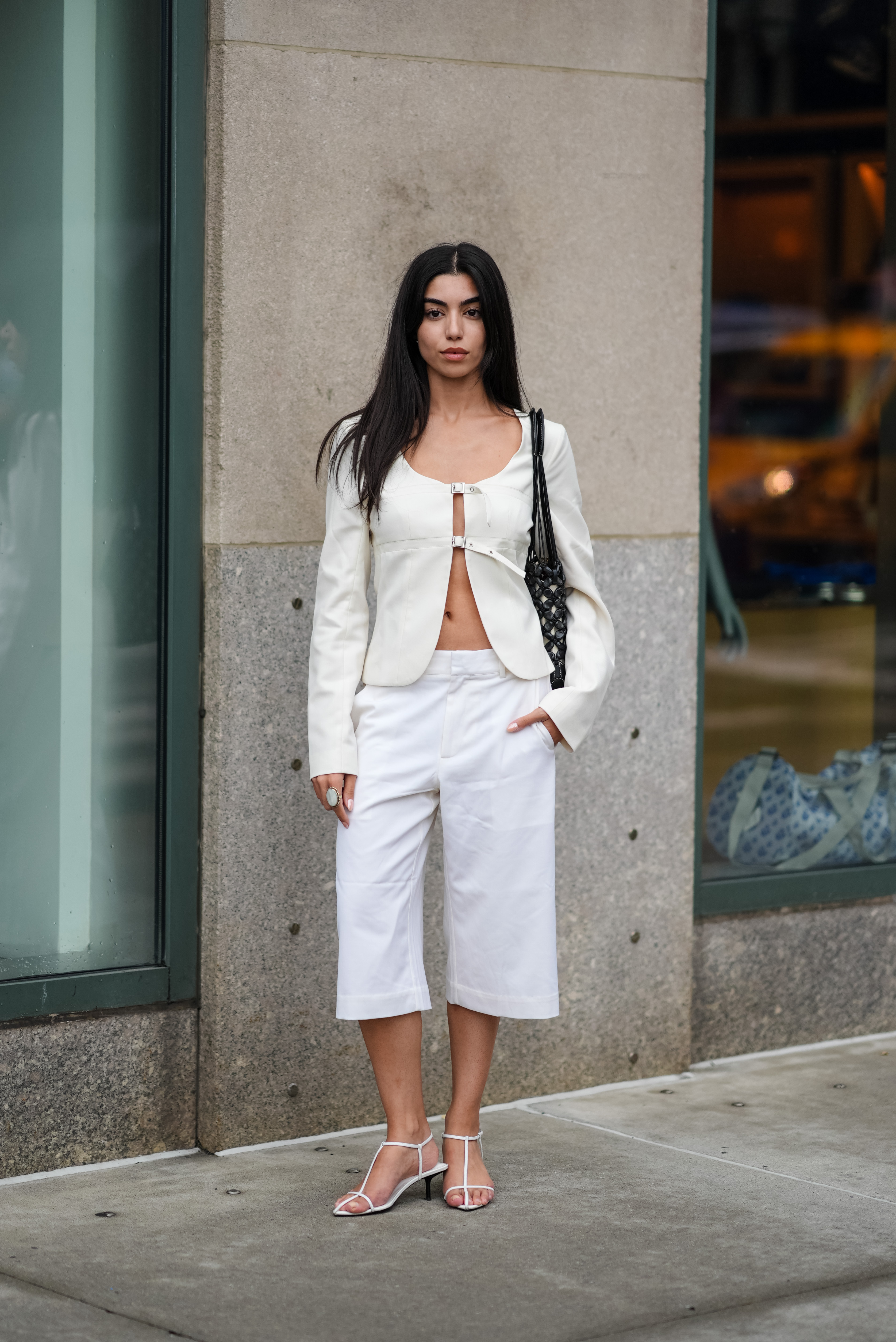 NEW YORK, NEW YORK - SEPTEMBER 07: A guest wears cream long sleeve shirt, black sheer mesh black leather bag, white capri pants, white sandals, outside Nanushka, during the New York Fashion week Spring/Summer 2025 on September 07, 2024 in New York, New York