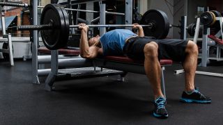 Man performs bench press exercise with barbell