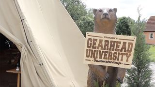 A brown bear holding a sign for Thomann's Gearhead University 2019 next to a tent