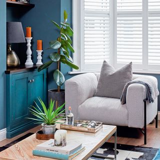 Teal living room with white armchair, wooden coffee table and white shutters