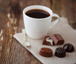 A cup of black coffee on a table next to Belgian chocolates