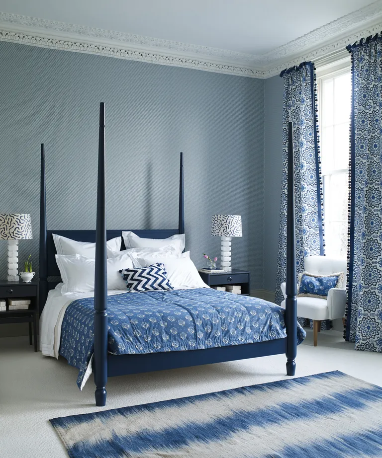 A bedroom with blue and white patterned wallpaper and a dark blue four poster bed