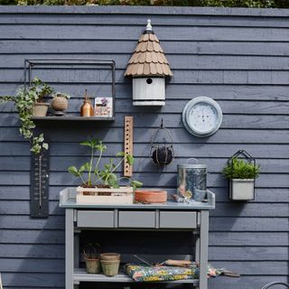 a potting table in a garden beside a grey painted fence