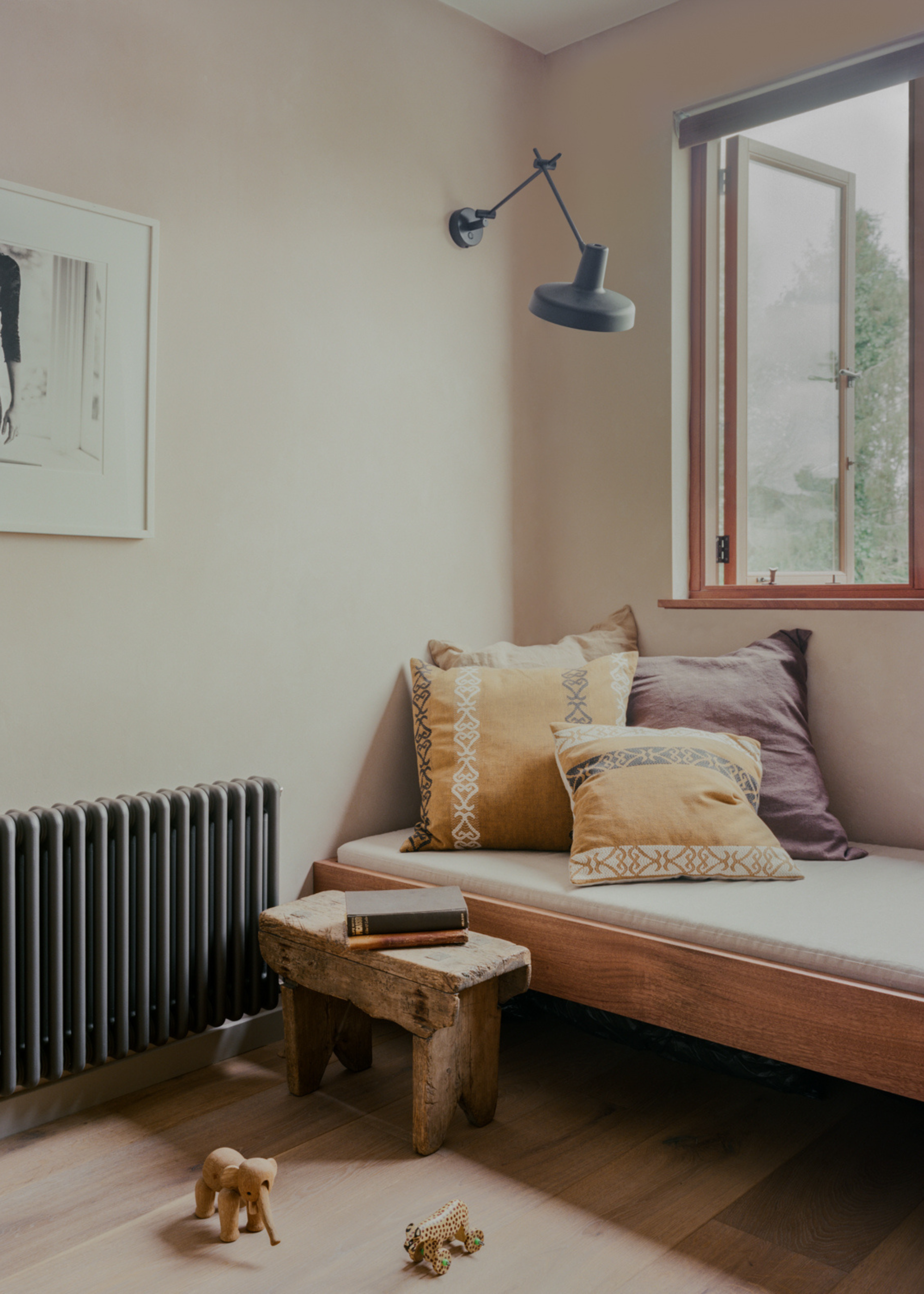 A meditation corner with patterned pillows, an upholstered bench, a wood stool, a heater, and an extendable black wall sconce