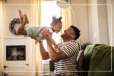 Father laughing as he swings happy child into the air from his position on a sofa at home