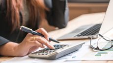A woman uses a calculator at her desk, only her hand showing.
