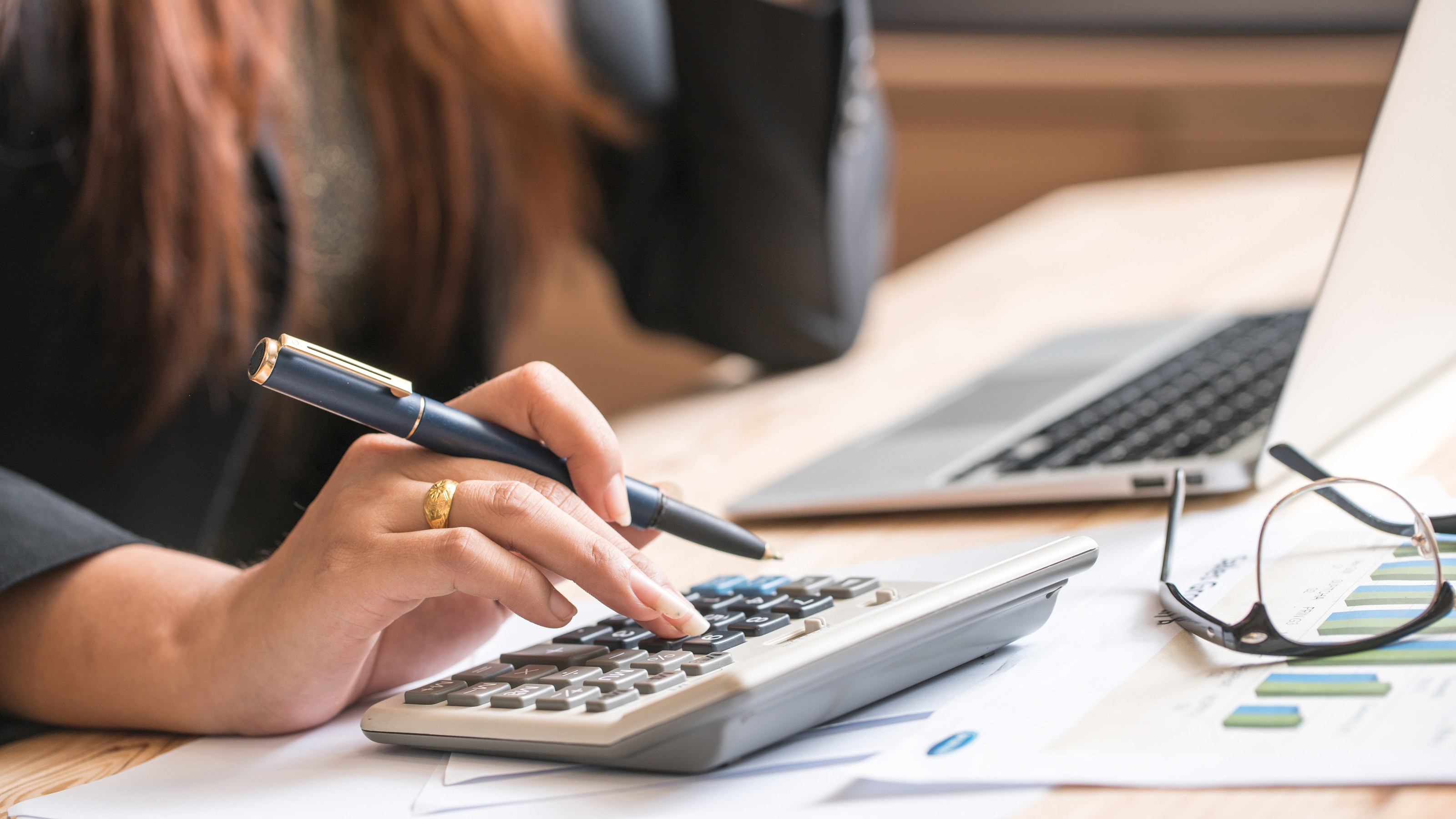 A woman uses a calculator at her desk, only her hand showing. 
