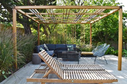 Wooden slat sun recliners in yard with pergola and simple planting scheme