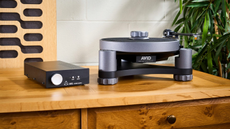 A lifestyle shot of the AVID Relveo turntable atop a wooden sideboard with a small amp beside it