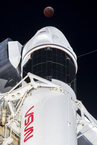 the reddish-brown moon is seen above a spacecraft atop a rocket.