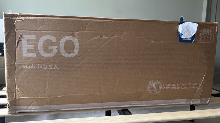The boxed-up EGOHOME Black 12" Mattress positioned on top of a wooden bed frame in a green bedroom.