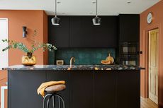 a stunning modern kitchen, with a dark island with marble multi-colored worktop, green tiles on wall behind, and peach walls everywhere else, with a wooden door