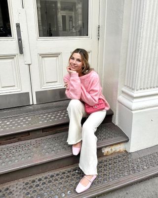 woman sitting on stoop wearing pink top, white jeans, pink Chanel quilted bag, pink Mary Jane shoes