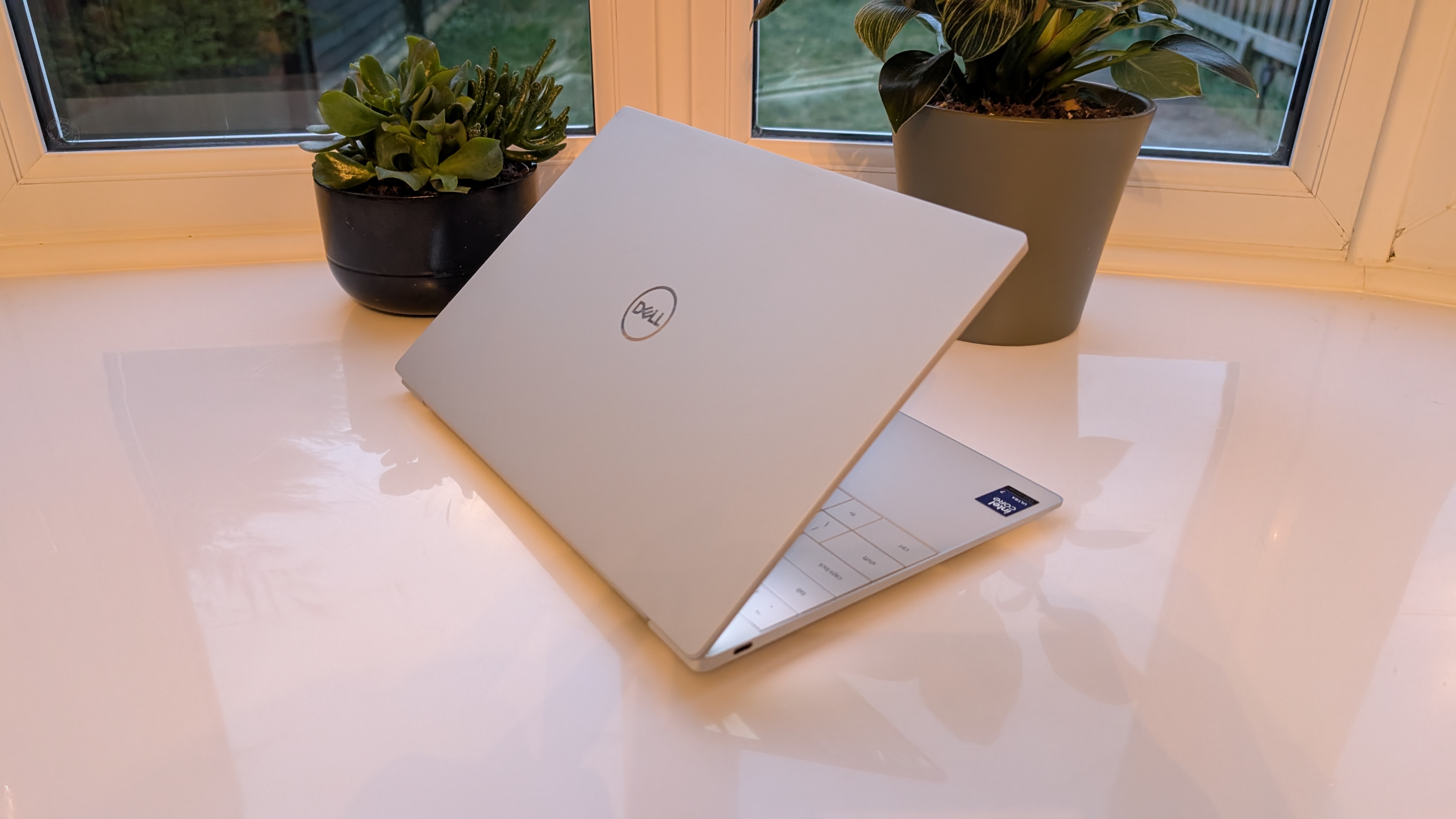 The Dell XPS 13 pictured on a white surface in front of a window with two potted plants.