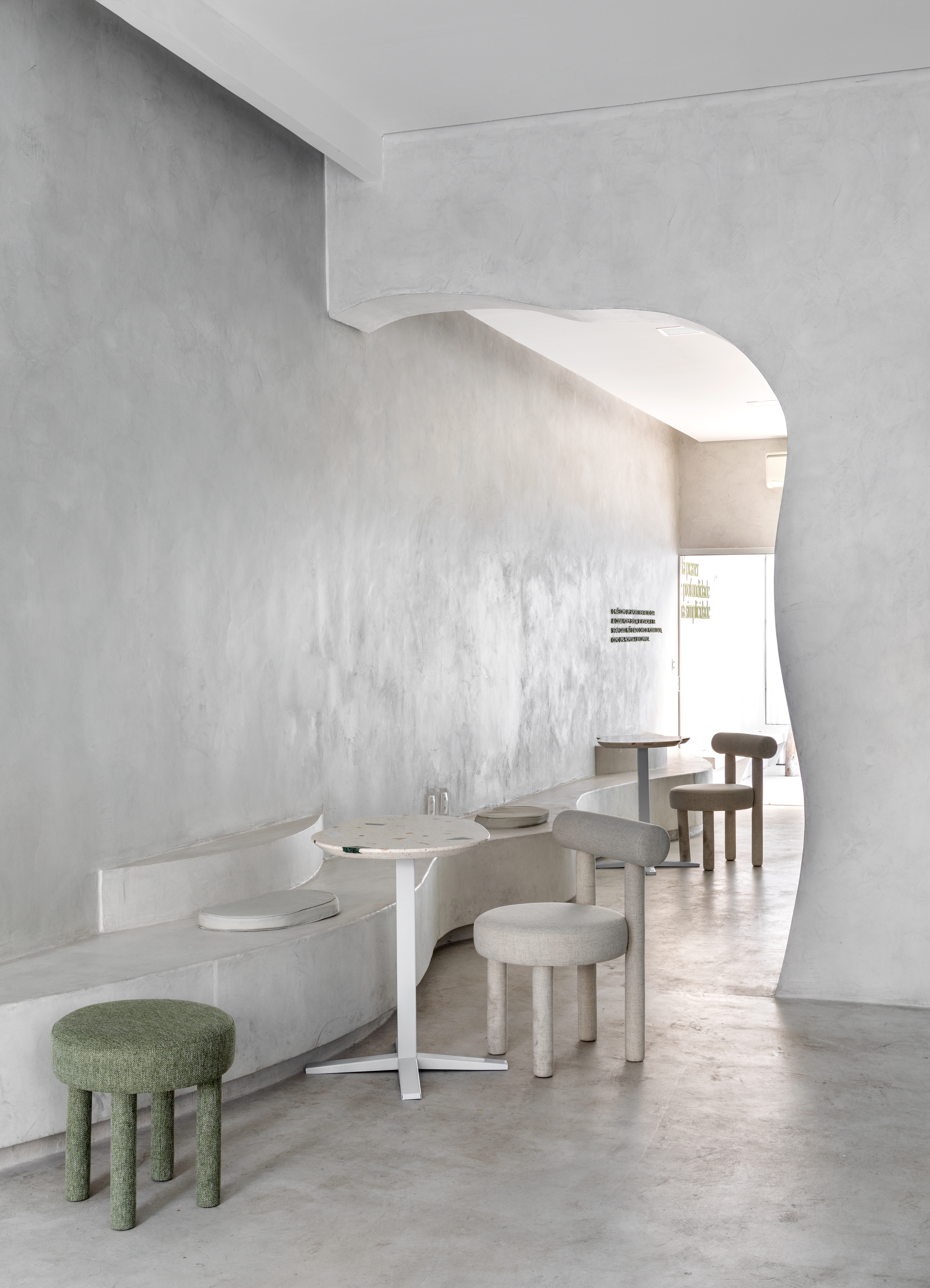 A white-washed, plastered matcha cafe with sculptural decor features monochromatic furnishings and an emerald green and chrome bar counter.