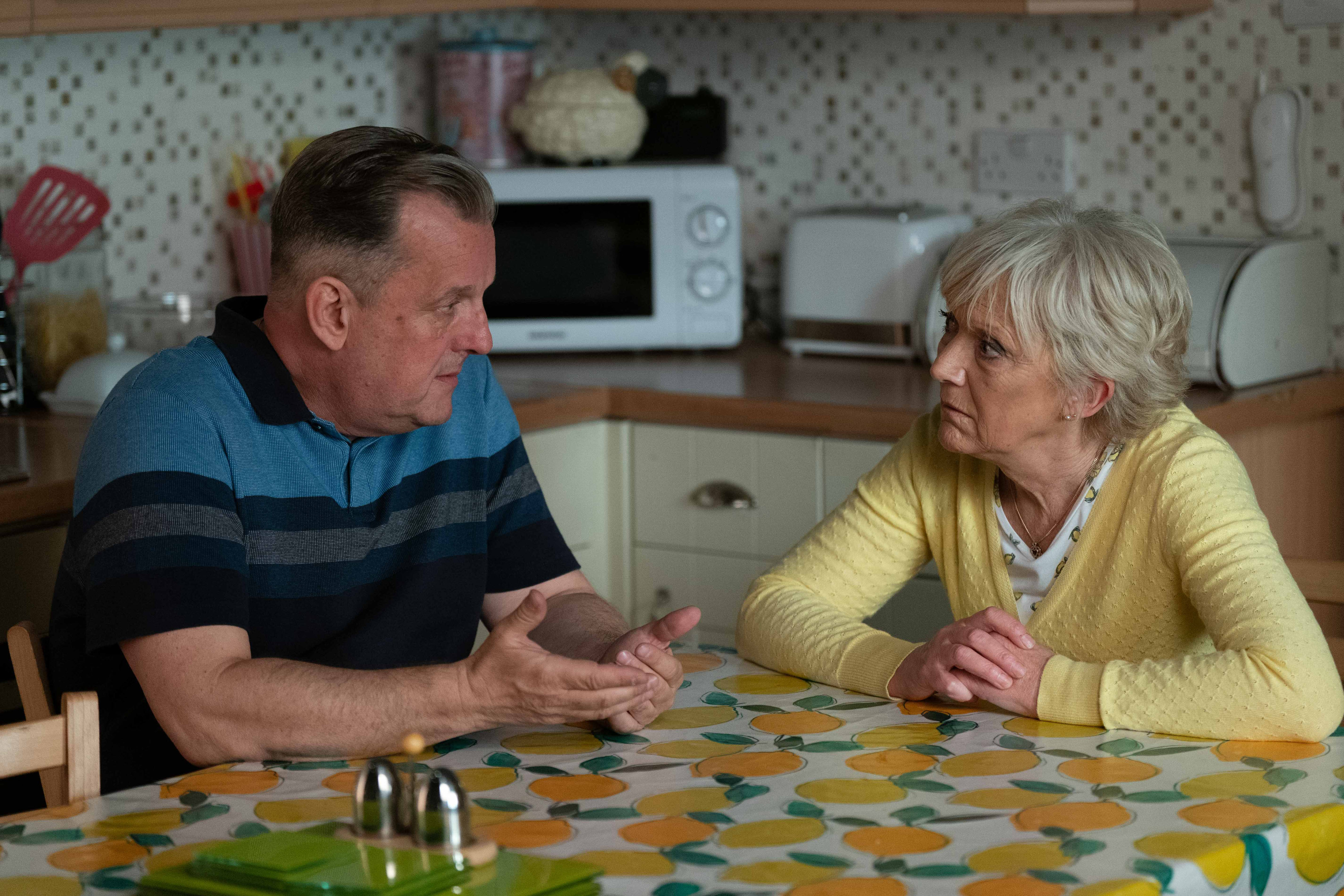 Harvey Monroe and Jean Slater talking at the kitchen table.