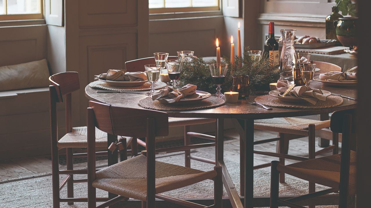 A dining table with mid-century modern dining chairs set for Christmas dinner with lit dinner candles