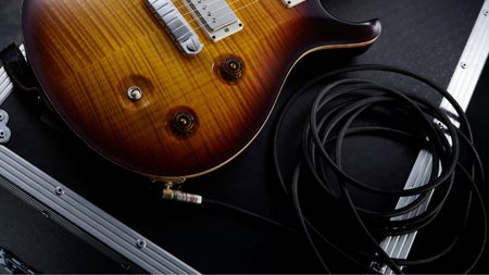 A PRS guitar on a flight case with a guitar cable plugged in