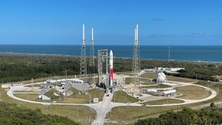 a red and white rocket stands on a launch pad with the ocean in the background.