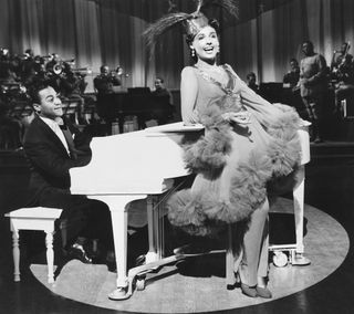 a woman in a feather dress sings while sitting on a piano in a still from Stormy Weather