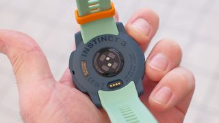 Close up of Garmin Instinct 3 GPS smartwatch in Neotropic/Twilight with a grey and orange case and sea foam green strap