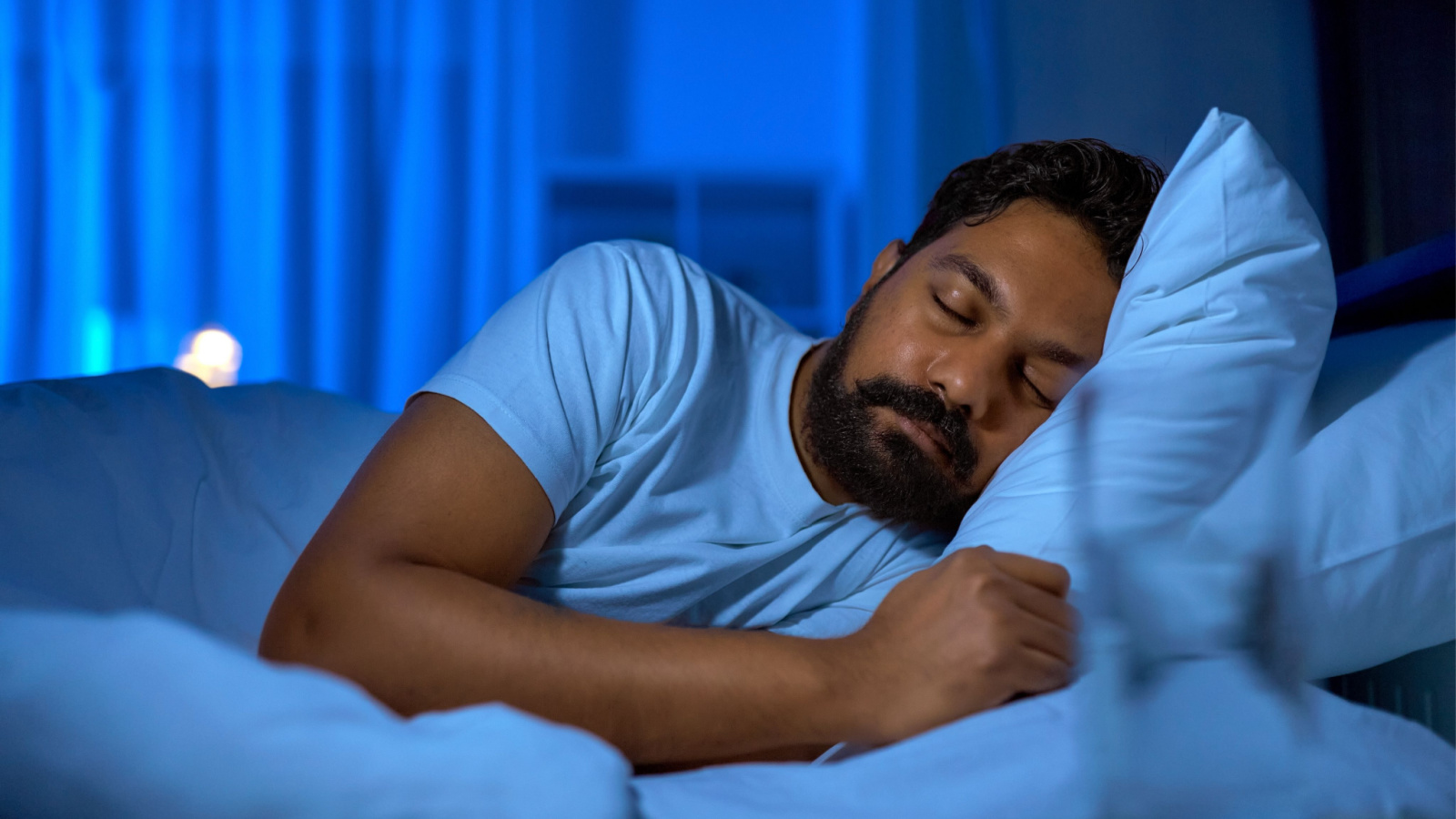 How to get a good night's sleep naturally, featuring a man sleeping on his side with his back to a window