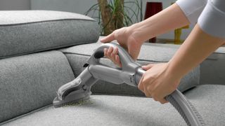 A vacuum cleaner with the upholstery attachment being used to clean upholstery
