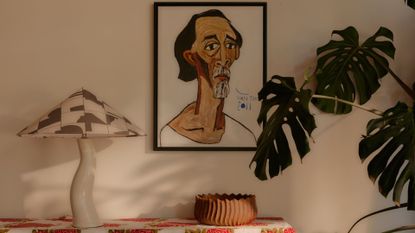 A monstera plant near a wavy desk lamp, a bowl and a framed artpiece