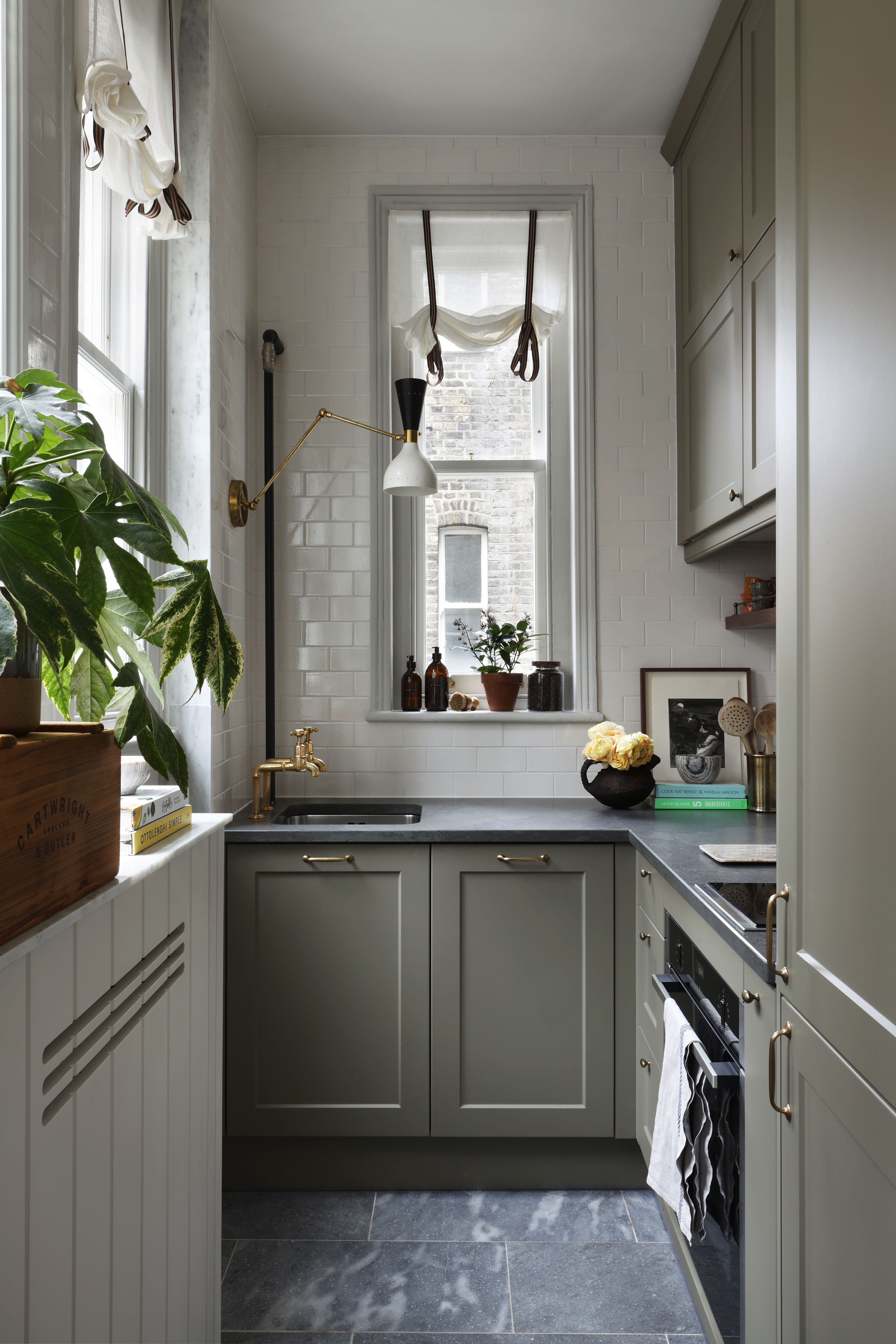 A narrow kitchen with olive cabinets, and a swing arm light