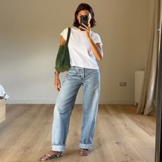 British style influencer Marianne Smyth poses for a mirror selfie wearing a white t-shirt, cuffed jeans, a green suede tote bag, python strappy sandals