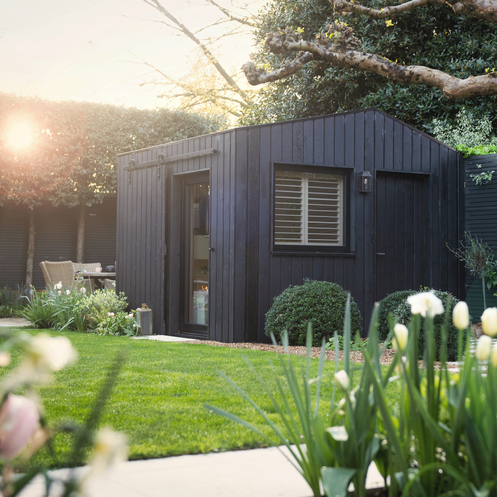 a garden with a patio area and black wood clad garden building and dining seating