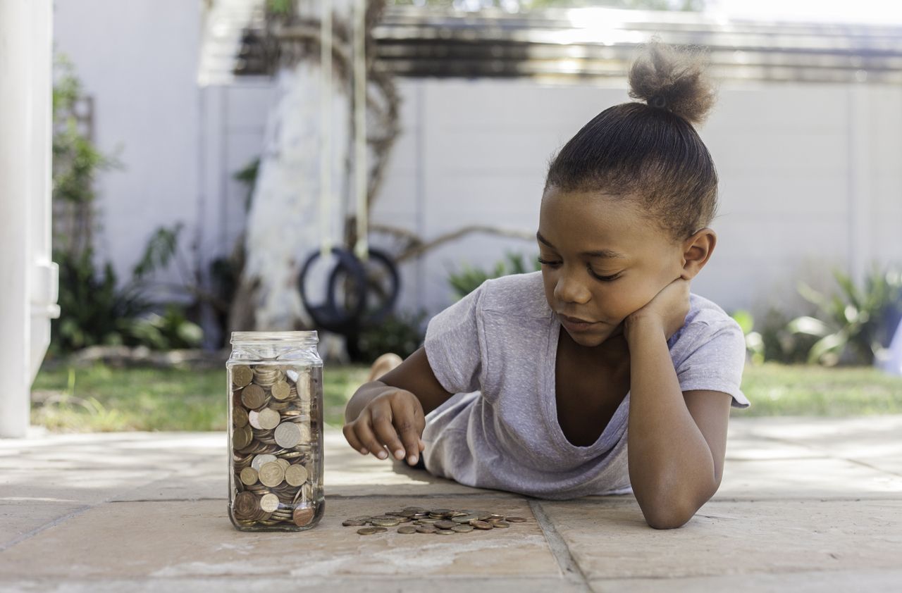 Young african female lying on the floor with a jar filled with coins counting how much she saved.