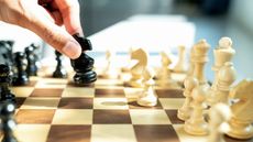 A man makes a chess move, only his fingers and the chessboard showing.