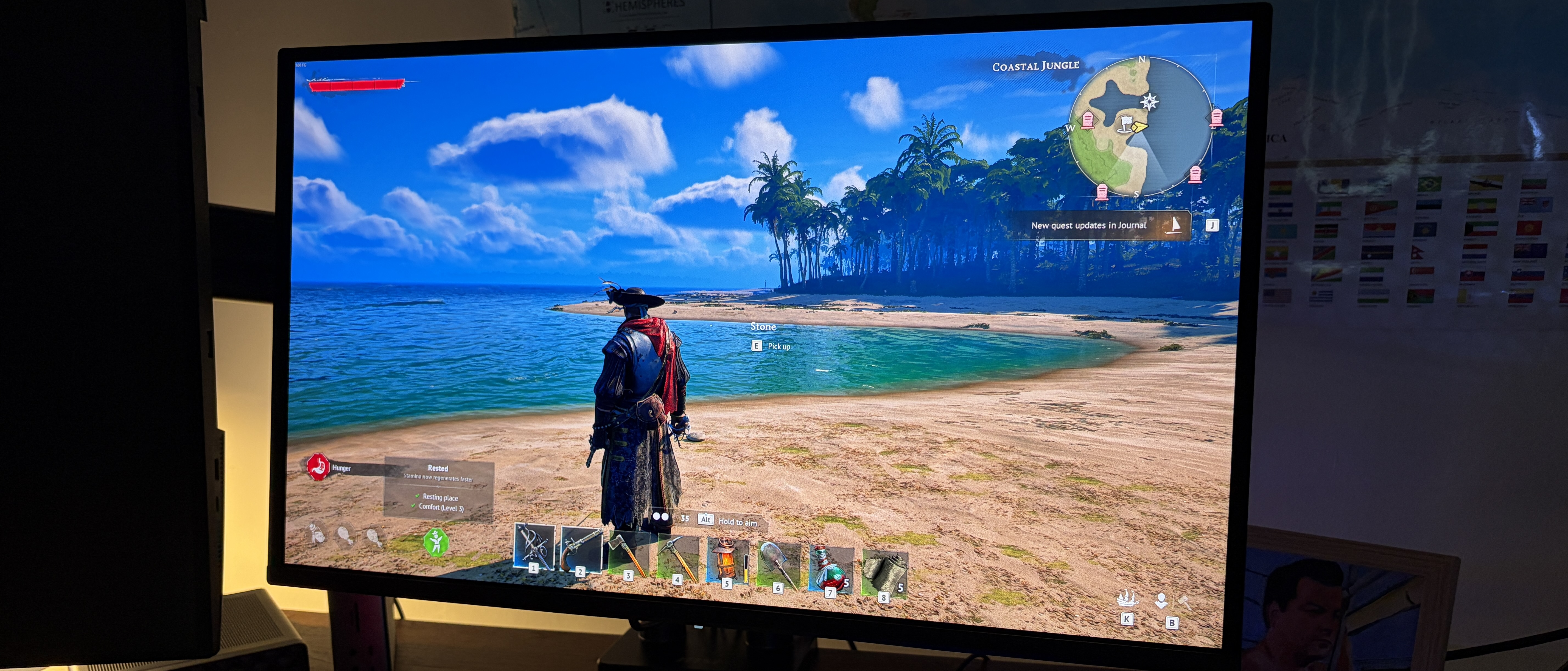 A computer monitor displays a video game with a pirate character standing on a sunny beach, overlooking the ocean. A detailed map is shown in the top-right corner.