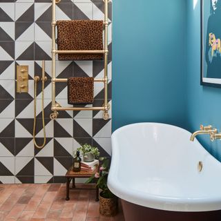 bathroom with blue walls and monochrome tile feature oil, towel rail and free standing bath and terracotta tiles underfoot