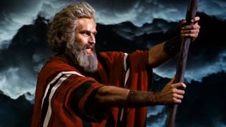 Charlton Heston as Moses holds a cane in front of thunderstorm clouds in The Ten Commandments