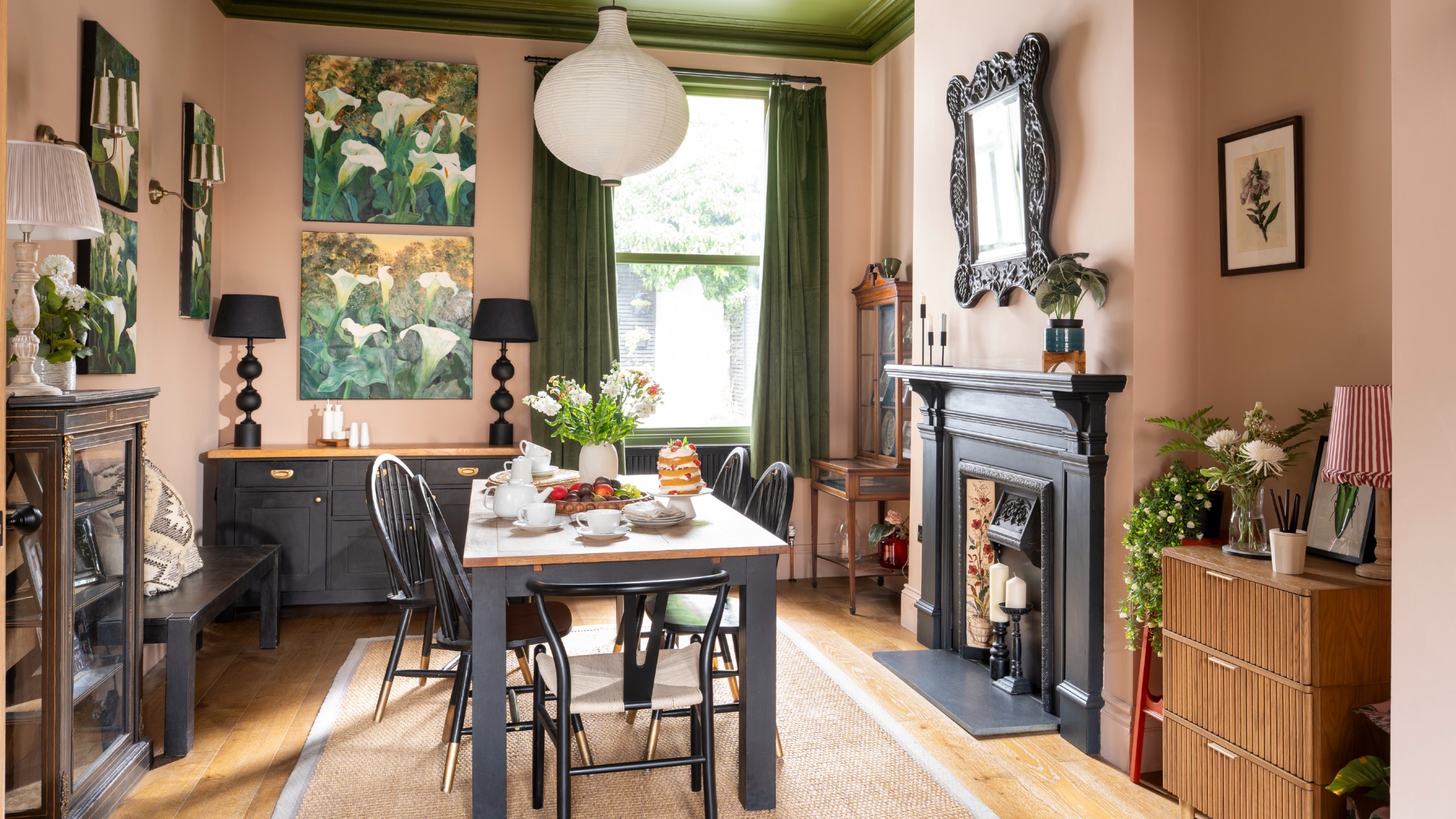 A pink-painted dining room with a contrasting green ceiling and black wooden dining table and chairs
