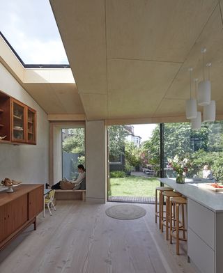 An open plan kitchen with a white island counter, a wooden console, a sitting alcove, a skylight, and large sliding doors.