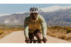 A man in a yellow windbreaker and white helmet rides towards the camera wearing the Rapha Dalton sunglasses
