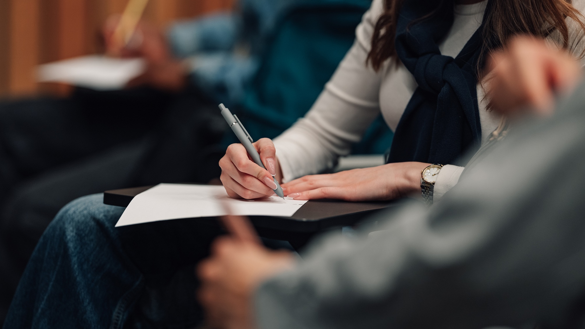 A person takes notes at a lecture, only their hands and paper showing.