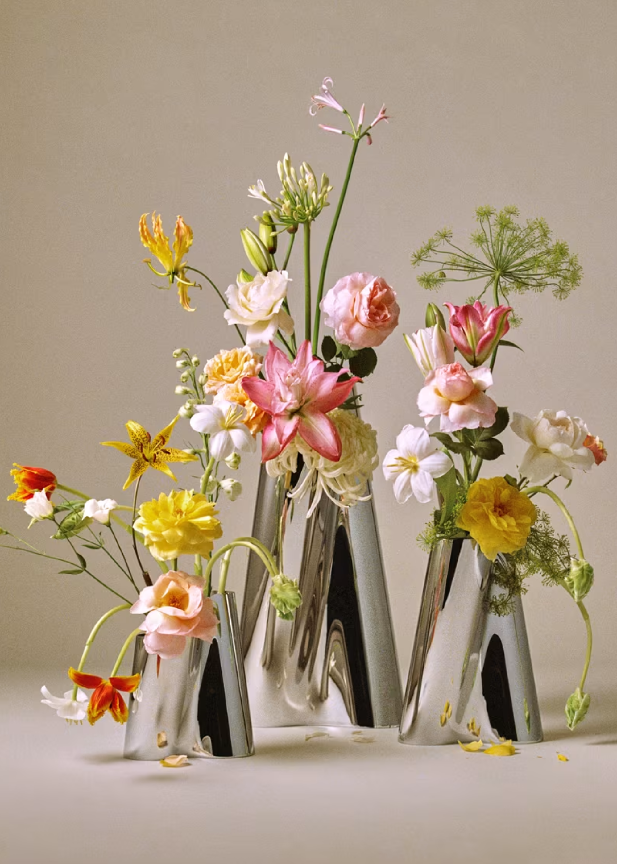 A trio of metallic chrome vases with colorful flowers
