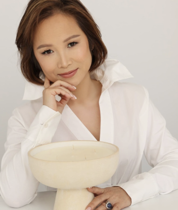 a headshot of a woman with short, brown hair wearing a white button down blouse and posing in front of a large candle