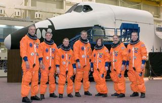 Astronauts in their orange spacesuits prior to launch of the Space Shuttle Atlanis on mission STS-125, in front of a mockup of the shuttle.