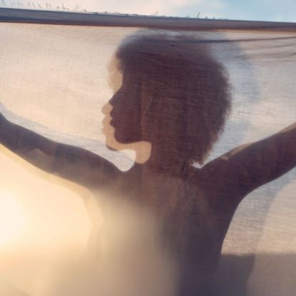 A shadow of a woman holding up a sheet to the sunlight