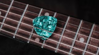 Turquoise guitar pick tucked under acoustic guitar strings